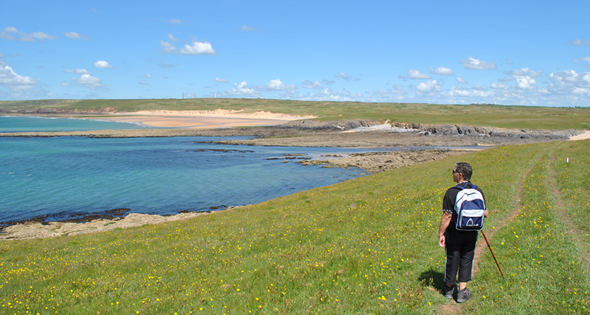 Person in hiking gear on a footpath on the Castlemartin Range, Pembrokeshire, Wales looking across a rugged coastline to a sandy beach in the distance