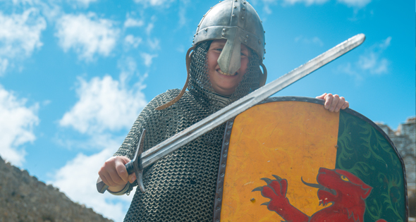 Child wearing medieval night costume including helmet and chainmail holding sword and shield at Carew Castle, Pembrokeshire, Wales, UK